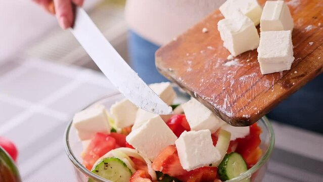 greek salad preparation series concept - woman pouring sliced feta cheese into a bowl