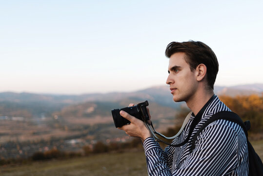 Man photographer with backpack and camera taking a photo of landscape in mountains.