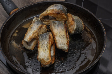 The cook fries carp fish in a frying pan on an induction stove	