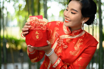 Asian pretty Chinese woman in cheongsam holding envelopen inside a Red amulet bag