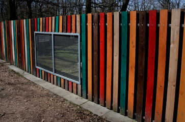 colorful striped wooden fence with a window for watching animals in the corral of the zoo park. mesh window for a safe view of the corral with goats. Galvanized mesh, garden yard
