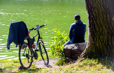 A man with a bicycle is sitting on the shore of a lake