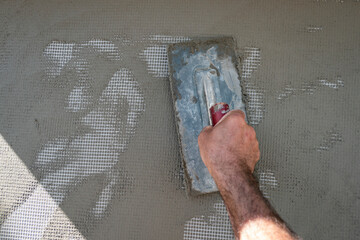 Trabalhador a colocar cimento com uma espátula na parede para rebocar a mesma
