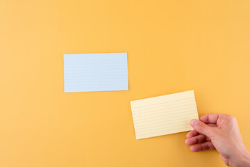 hand putting blank writing paper and empty paper on a yellow background. space for text.