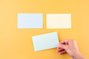 hand putting blank writing paper and two empty papers on a yellow background. space for text.