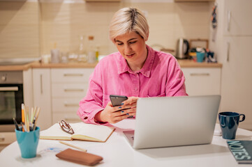 Woman with short hair using her smartphone and a modern laptop at home