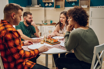 Group of friends enjoying dinner while sitting at the kitchen table together