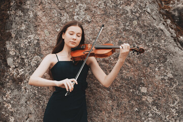 Asian girl plays the violin on the background of a stone wall © Fotograf