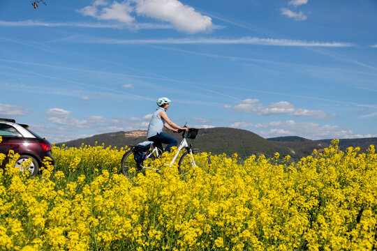 Frau fährt mit Fahrrad durch blühendes  Raps Feld, Frühlingsanfang mit Sonnenschein und blauem Himmel.