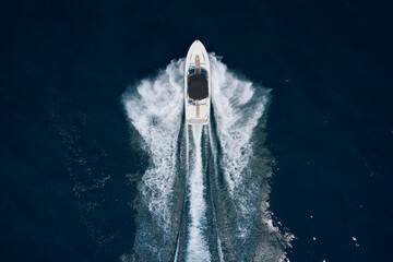 Speedboat on dark water aerial view. White boat with a black awning movement on the water drone view. Boat trip at sea. - obrazy, fototapety, plakaty