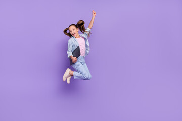 Photo of pretty excited little school girl wear denim shirt jumping holding modern device empty...