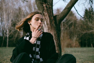 portrait of a girl sitting in the park and happily smoking marijuana