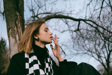 portrait of a girl sitting in the park and happily smoking marijuana