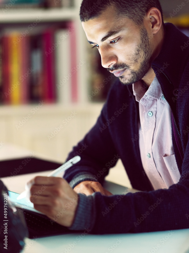 Poster getting down to the task at hand. shot of a focused young man working on a digital tablet in his hom