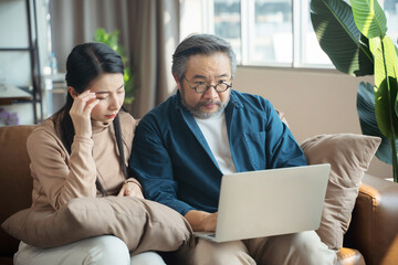 Serious stressed Middle-aged Asian couple finances calculate bills tax on the laptop.