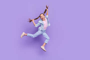 Fototapeta na wymiar Photo of pretty funky little school girl wear denim shirt jumping high holding tails empty space isolated purple color background