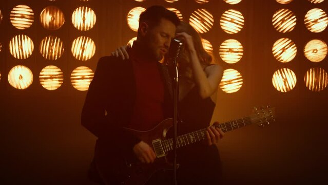 Attractive guy playing guitar with girl dancing in club. Couple enjoying music