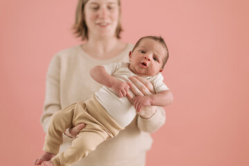 photo of a newborn baby held in hands by mom over pink background