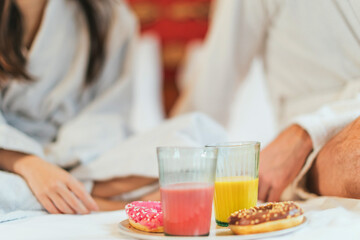 breakfast in bed - details on juices and donuts - people in a bathrobe