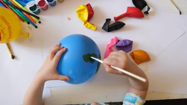 Child making planet for earth day from balloon. drawing blue ball with green continents. Protection of environment, Save our planet. Ecology concept. art learning and education love earth save world