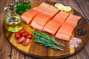 Pieces of salmon fillet with spices and olive oil on a wooden board.