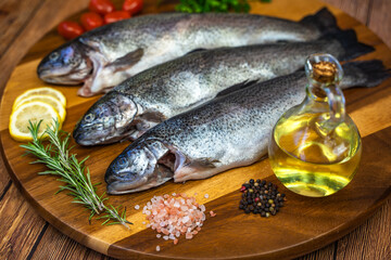 Three raw trout with spices and olive oil on a wooden board.