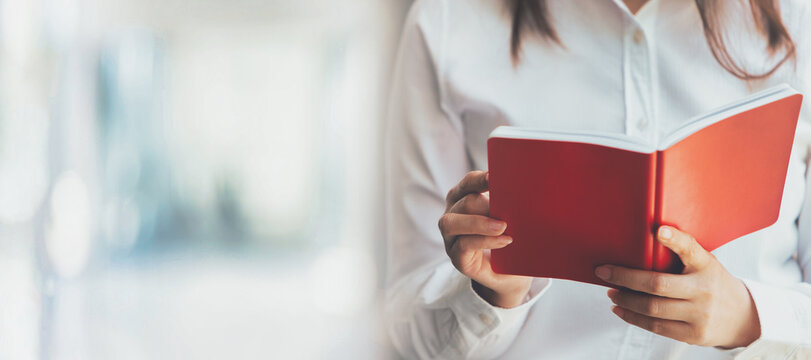 Close-up of female hands opening a red notebook, panoramic banner background with copy space