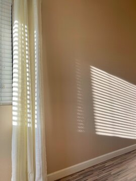 Sunlight streaming in through window blinds making a pattern on the wall