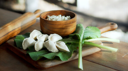 Russian fresh handmade dumplings lying on a wooden table on a cutting board with cottage cheese in a wooden plate and spinach