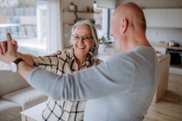 Cheerful senior couple dancing together at home.