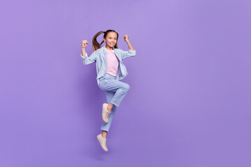 Fototapeta na wymiar Photo of excited pretty little school girl wear denim shirt rising fists jumping high empty space isolated purple color background