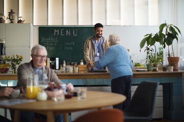 Young caregiver serving breakfast to elderly woman in nursing home care center.