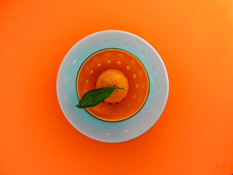 Overhead view of a satsuma in an orange dish on an orange background