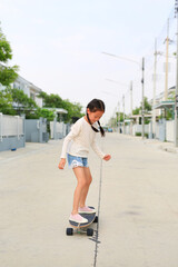 Asian little young girl child skating unsafe without protection on skateboard at the street