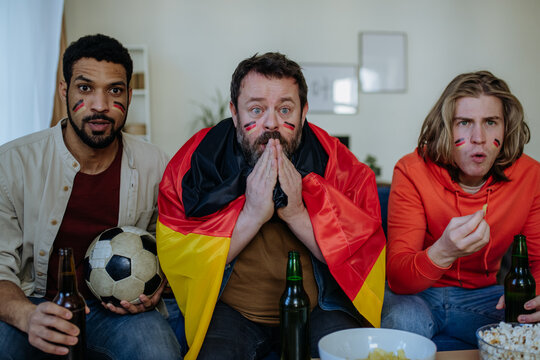 Nervous football fans friends staring at TV and watching football match at home
