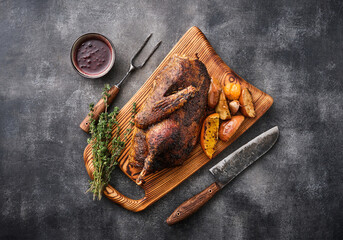 Half goose with sauce and apples baked on a wooden board with a knife and fork against a gray...