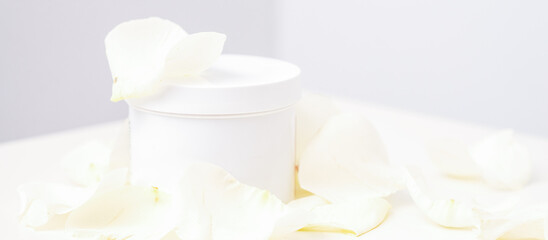 Fototapeta na wymiar White jar with cream among delicate white rose flowers petals on a light background. Natural organic cosmetics concept, close up, mock-up