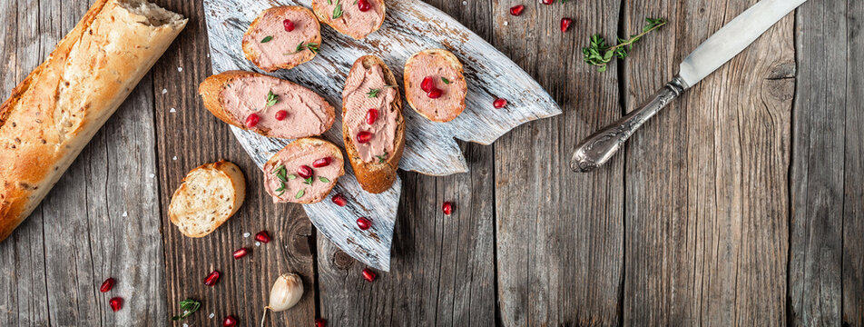 gourmet Belgian duck liver pate bread on a wooden background. Fresh homemade chicken liver pate on toasted bread with greens and pomegranate. Long banner format. top view. place for text