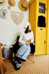 Young woman in beret sits in an armchair in cozy home, in room with music record in hands. Vintage yellow cabinet. Home interior