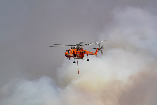 Bundoora, Australia - December 30, 2019: Erickson Air Crane helicopter flying against plumes of smoke while fighting bush fires in Victoria, Australia.