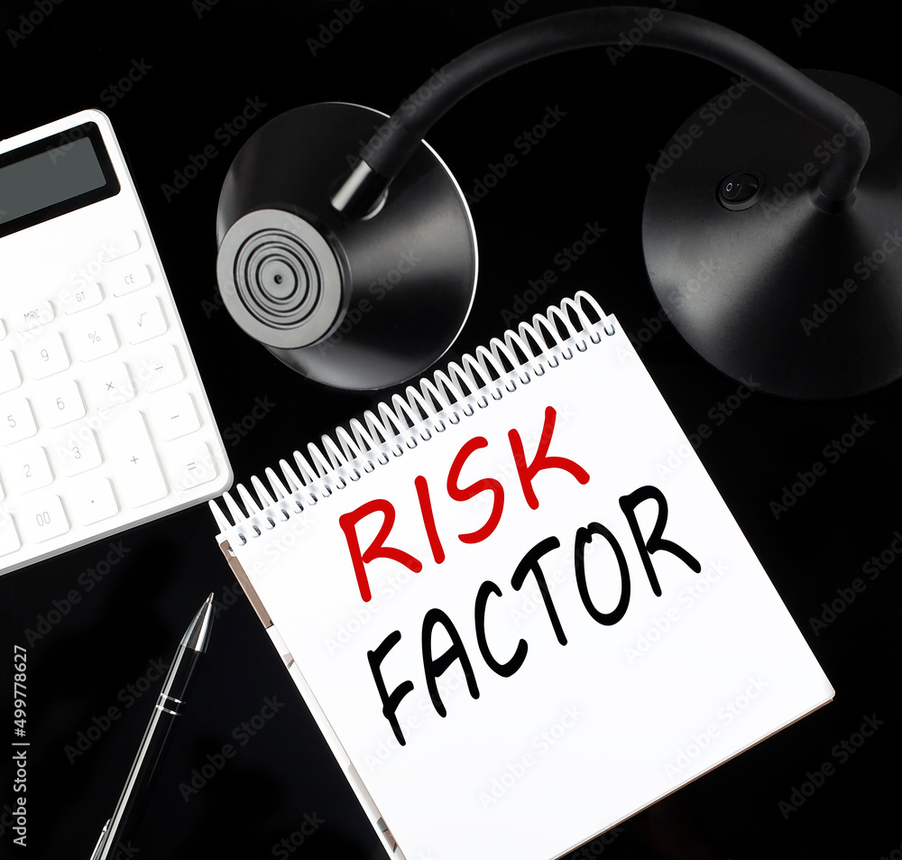 Aufkleber opened paper notebook with text risk factor with a pen, calculator and table lamp on black backgroun