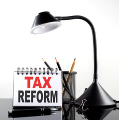 TAX REFORM text on notebook with pen and table lamp on the black background