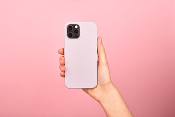 Fototapeta Female hand holding white smartphone in soft silicone cover back view . Phone case mock up isolated on pink background obraz