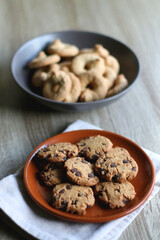 Plate of chocolate chip cookies and bowl of sugar cookies on wooden table. Selective focus.