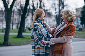 Naklejka premium A grandmother is touching her adolescent granddaughter's face with affection. They met in the park during cold weather.