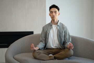 Focused Asian man meditates in Lotus pose breathing deep and slowly. Young male person in casual...