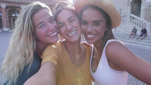 Three multi ethnic young female friends laughing together taking selfie outdoors - Multiracial women having fun on summer vacation in Italy - Unity happy people and friendship concept