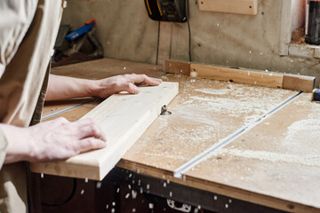 Unrecognizable carpenter shaping wood plank on benchtop router table in woodworking workshop - obrazy, fototapety, plakaty
