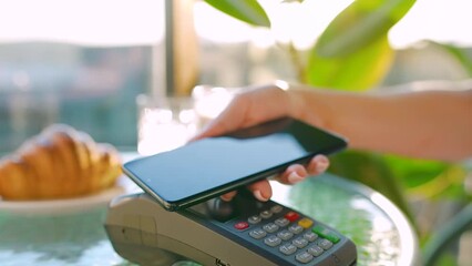 Contactless payment with smartphone. Wireless payment concept. Close-up, woman using smartphone cashless wallet NFC technology to pay order on bank terminal in a cafe.