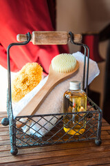 In the forged basket there are massage oil, a body brush and a bath towel against the backdrop of a beautiful retro interior. Massage and spa theme. Vertical photo.